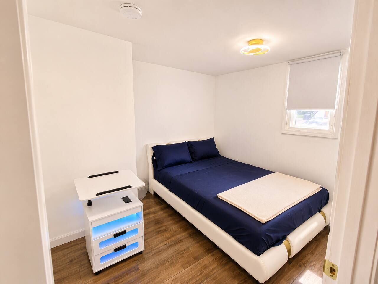 A small, compact bedroom with a single bed, a bedside table, and a storage unit with drawers.