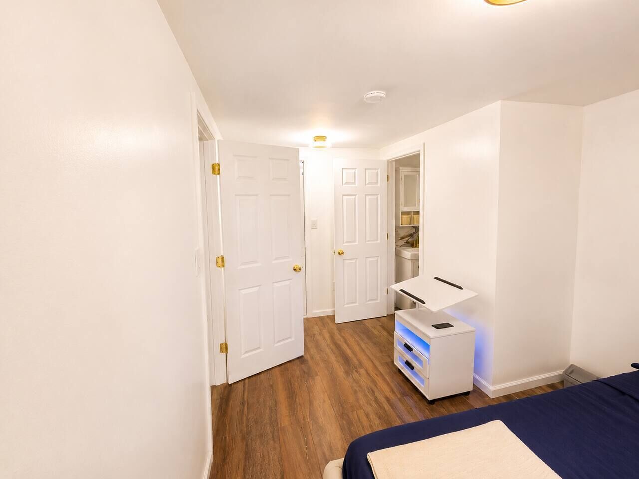 A bedroom with a bed, bedside table, and a dresser. There are two doors leading to other rooms.