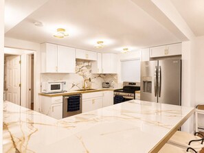 A modern kitchen with white cabinetry, a marble countertop, stainless steel appliances, and recessed ceiling lighting. - Lakeside Vista | 4 Seasons Waterfront Resort (Elkhart)