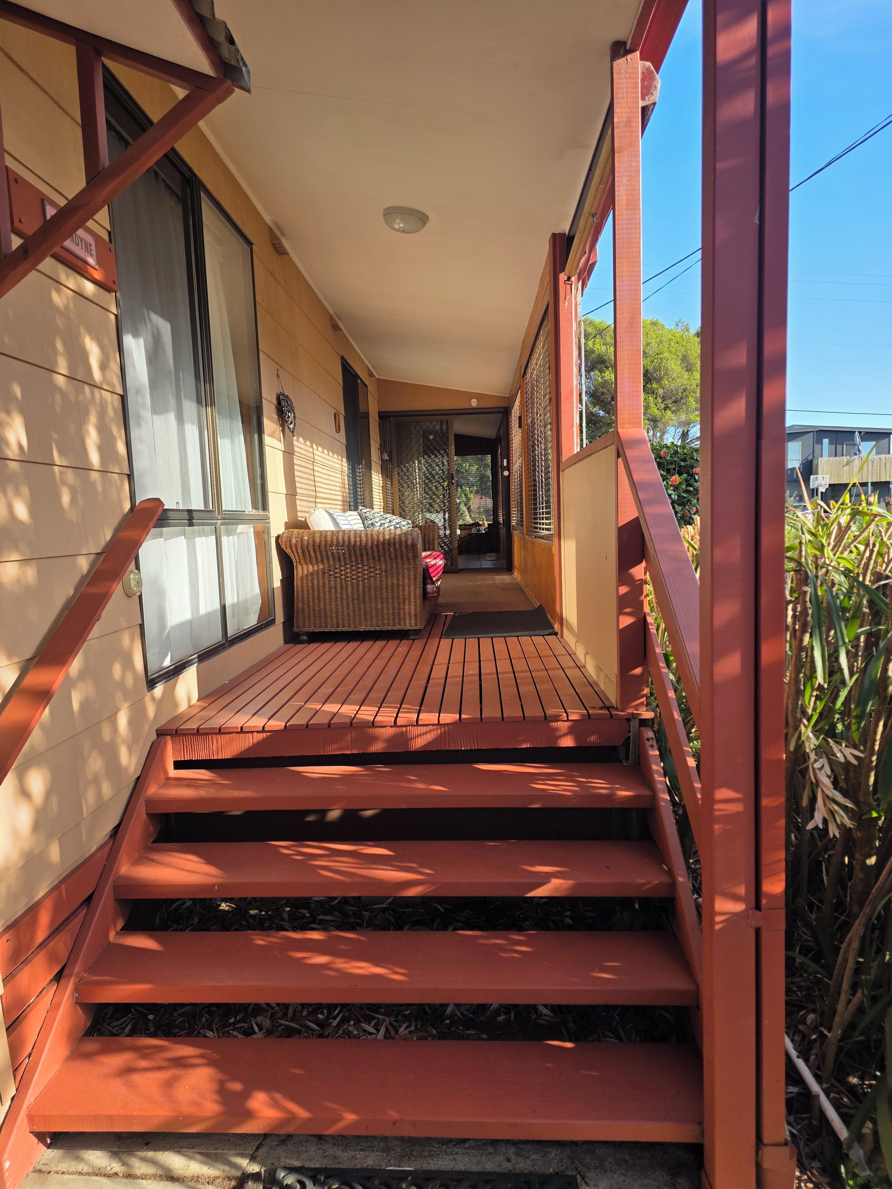 A wooden staircase leading to a covered outdoor area with a wicker sofa and a door leading to an interior space.