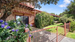 Ein Wohnhaus mit eingezäunter Garten, einer Holzpergola und vielfältigen Pflanzen.