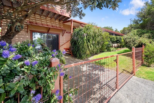 Una propiedad residencial con patio cercado, pérgola de madera y diversas plantas.