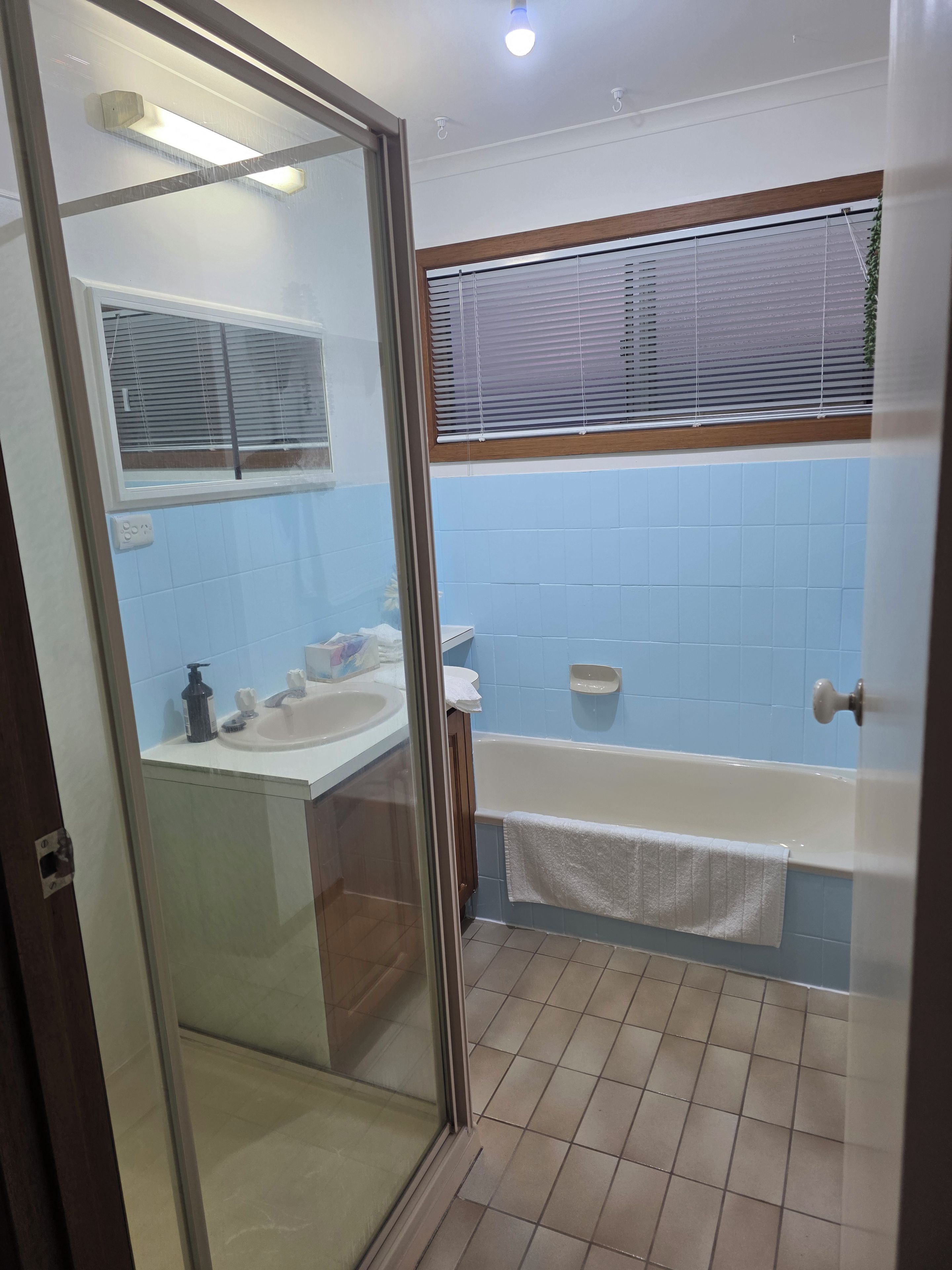 A bathroom with a glass shower enclosure, a white sink, a bathtub, and blue tiled walls.