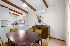 Un comedor con una mesa y sillas de madera, una cocina al fondo y un jarrón decorativo con flores sobre un mueble.