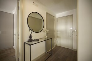 Un couloir avec un miroir posé sur une console, un vase rempli de fleurs et une porte donnant sur une autre pièce.