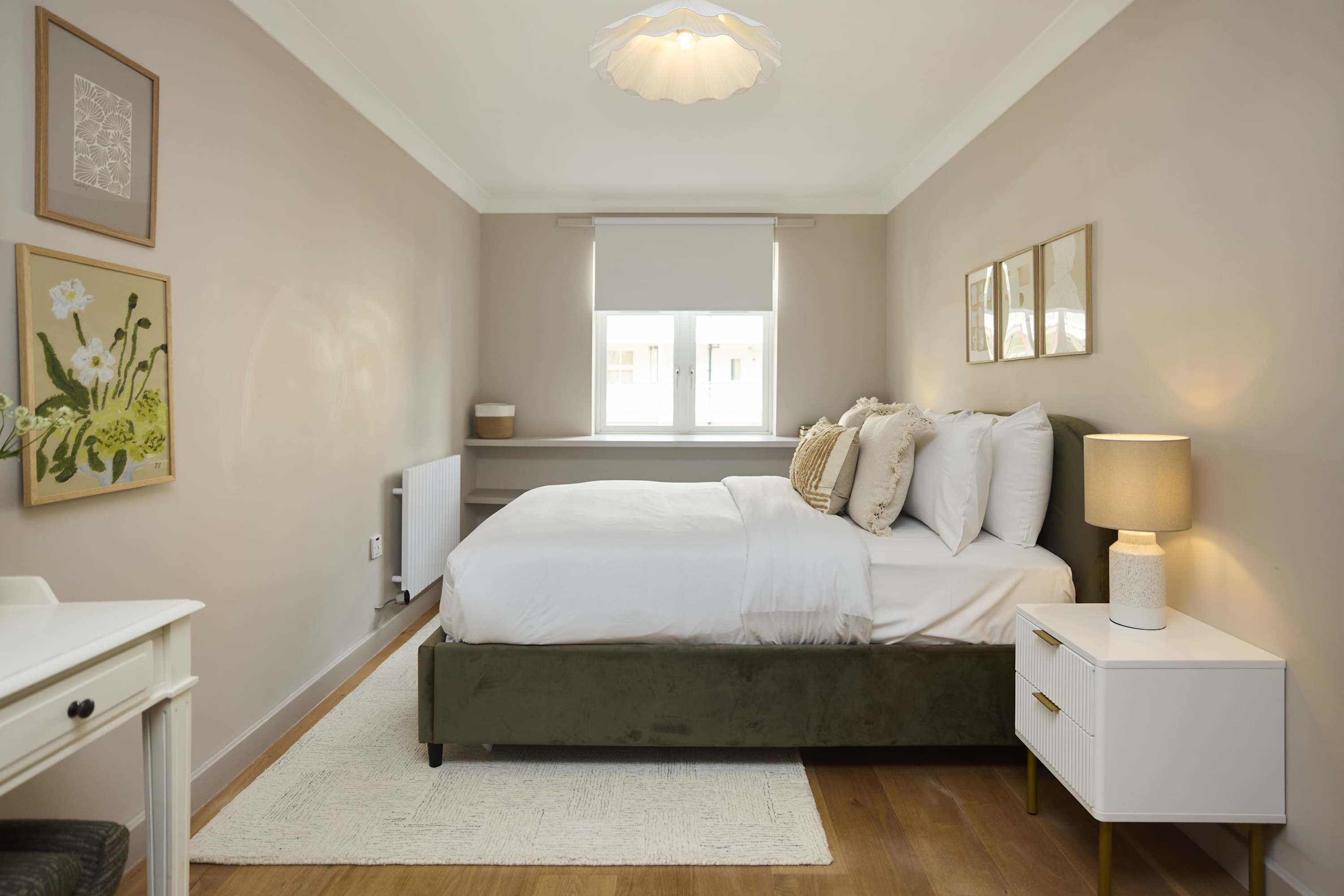 A bedroom with a bed, bedside tables, a radiator, a window, and artwork on the walls.
