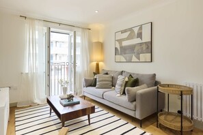 Un salon avec un canapé, une table basse, une lampe, un tableau et une fenêtre avec des rideaux.