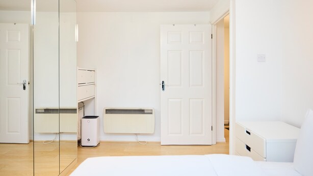 A minimalist bedroom with a bed, a wardrobe, a radiator, and a door. - Meet Me in Willesden Green (London)