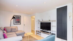 A modern living room with a sofa, a small table, a TV, and a black cabinet. - Meet Me in Willesden Green (London)