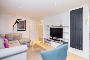 Ein modernes Wohnzimmer mit einer Couch, einem kleinen Tisch, einem Fernseher und einer schwarzen Kommode.
