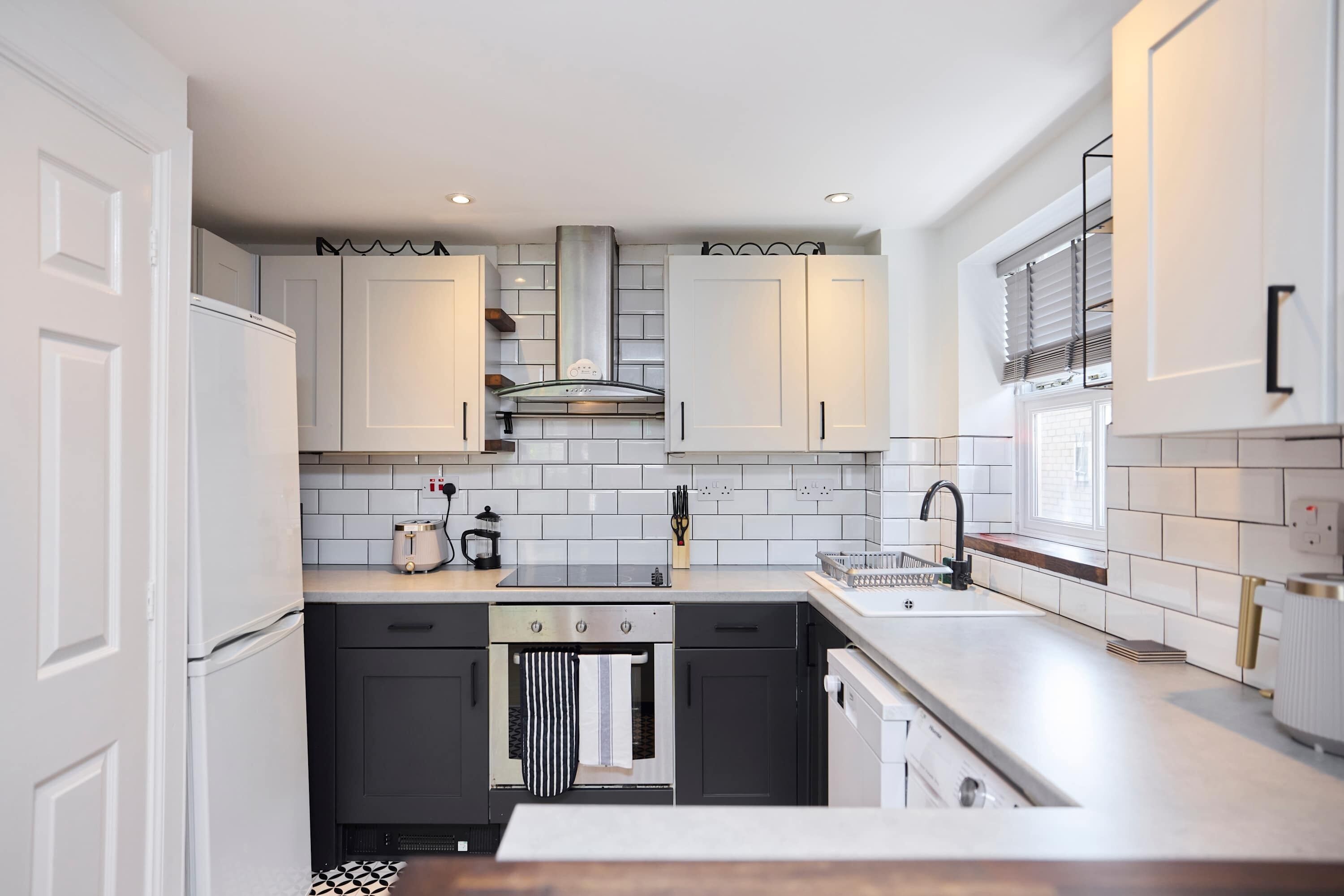 Une cuisine moderne avec des meubles blancs, une hotte en acier inoxydable et un four encastré.