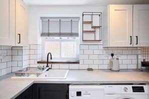 Eine moderne Küche mit weißen Schränken, einem eingebauten Geschirrspüler und einem Fenster mit Jalousien.