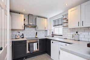 A modern kitchen with white cabinetry, a black and white tiled backsplash, and a patterned floor. - Meet Me in Willesden Green (London)
