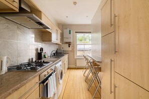 A modern kitchen with a gas stove, a built-in oven, a washing machine, and a window providing natural light. - Brick & Beam on Tabard (London)