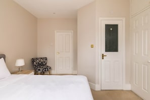 A hotel room with a bed, a chair, a nightstand, and a door. - Brick & Beam on Tabard (London)