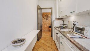 A narrow kitchen with white cabinets, a tiled floor, and a brick wall. - Apt. Annamaria: Family-Friendly 2BR Central Base for Trips, Laveno Mombello, Italy (Laveno Mombello)