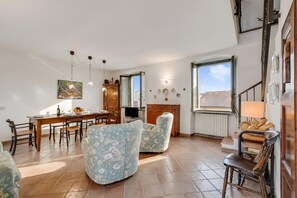 Ein Essbereich mit Holztisch und Stühlen, einem floralen Sofa und einer Küchenzeile mit Herd und Schränken.