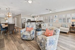 A modern living room with a sofa and armchairs, a dining area with a table and chairs, and a kitchen in the background. - Luxury Oceanfront Vacation w/ Pool (Indian Rocks Beach)