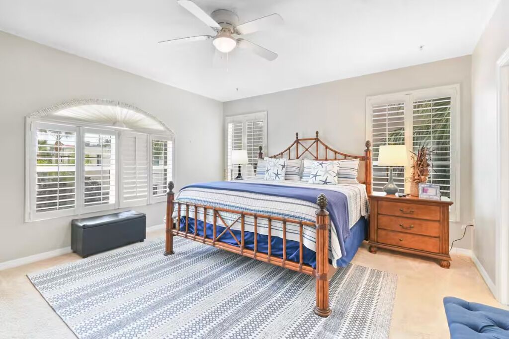 Un dormitorio con cama, cómoda, mesita de noche, ventilador de techo y ventana con contraventanas.