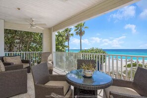 Ein überdachter Außenbereich mit Korbmöbeln und einem Tisch, mit Blick auf einen Strand mit Palmen und dem Meer.