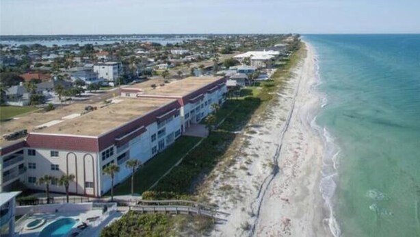 Vista aérea de una propiedad costera con playa, un edificio grande de techo rojo y una vista despejada del océano.