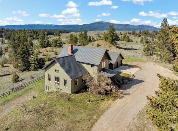 A two-story house with a metal roof, surrounded by a fenced yard and a dirt driveway.
