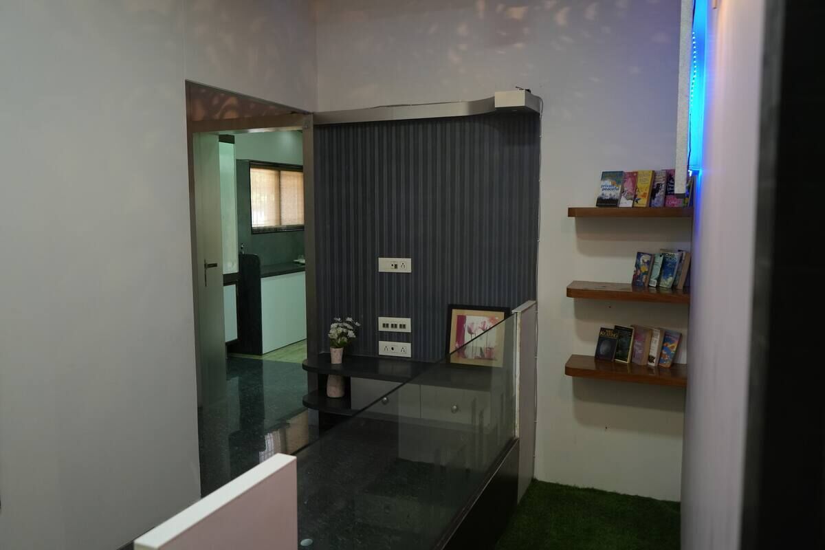 A modern interior with a glass staircase, a dark wall unit with books, and a green carpeted area.