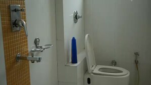 Et badeværelse med toilet, hårtørrer og en blå flaske på en hylde.