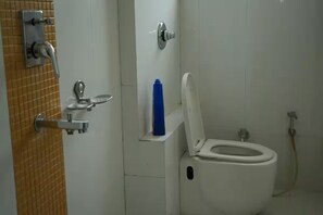 Ein Badezimmer mit Toilette, einem Händetrockner und einer blauen Flasche auf einem Regal.