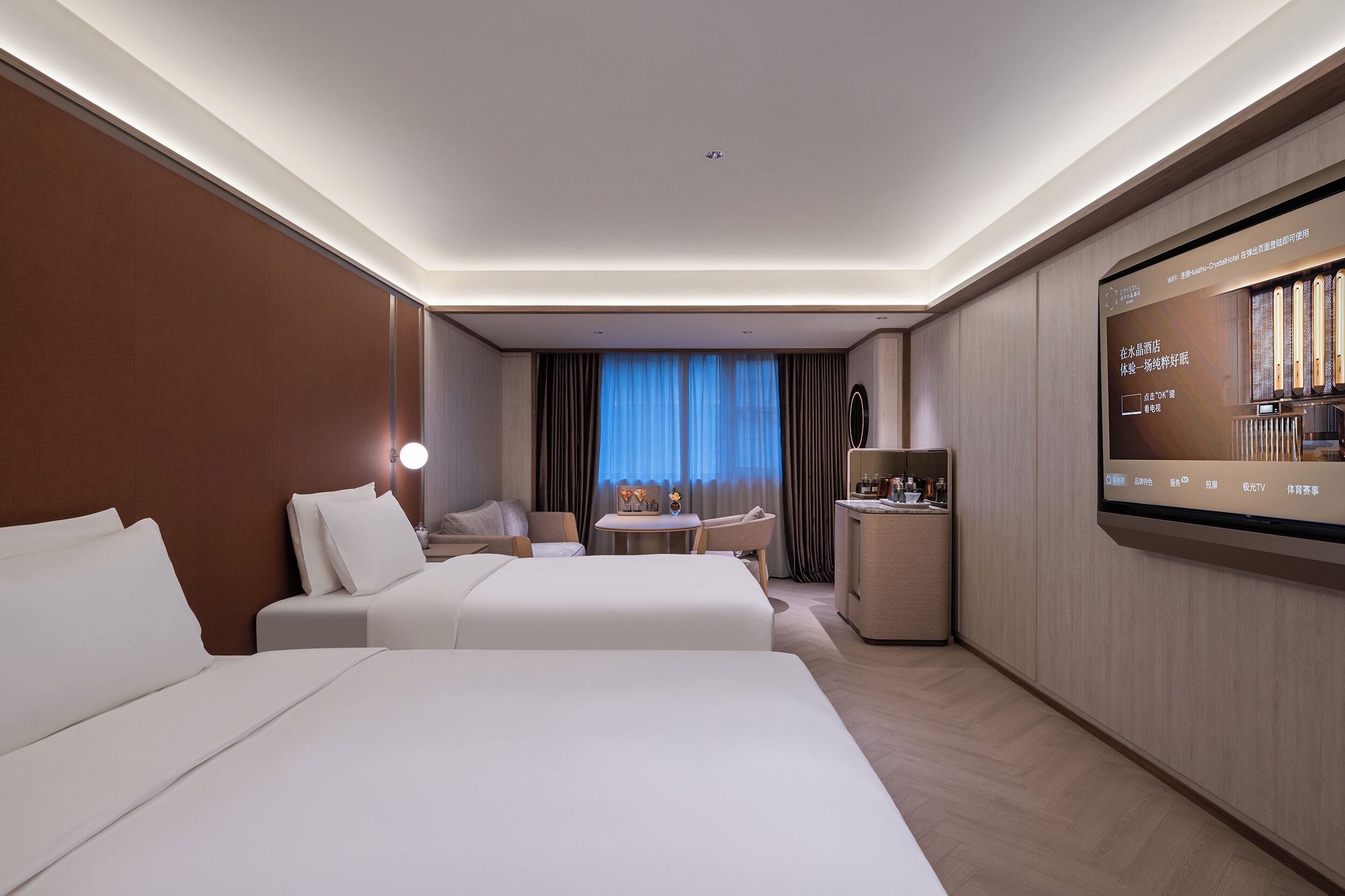 A hotel room with two beds, a desk, a chair, a TV, and a minibar.