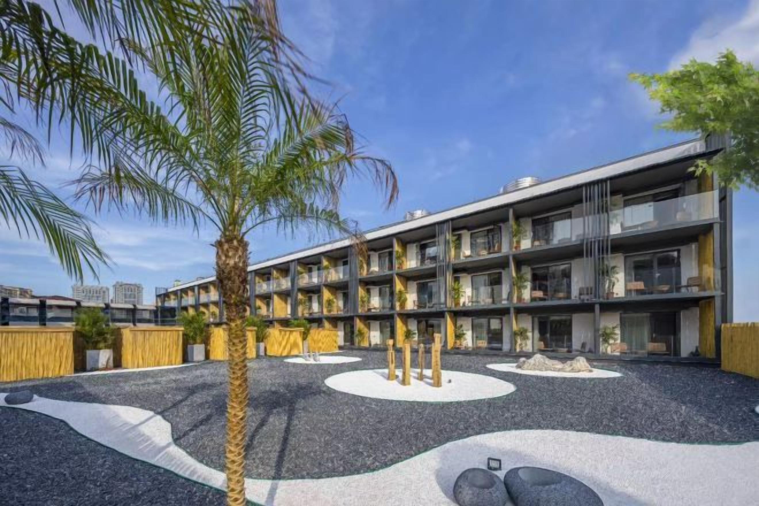 A modern building with multiple floors, outdoor seating area, and palm trees.