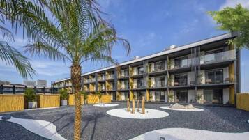 A modern building with multiple floors, outdoor seating area, and palm trees.