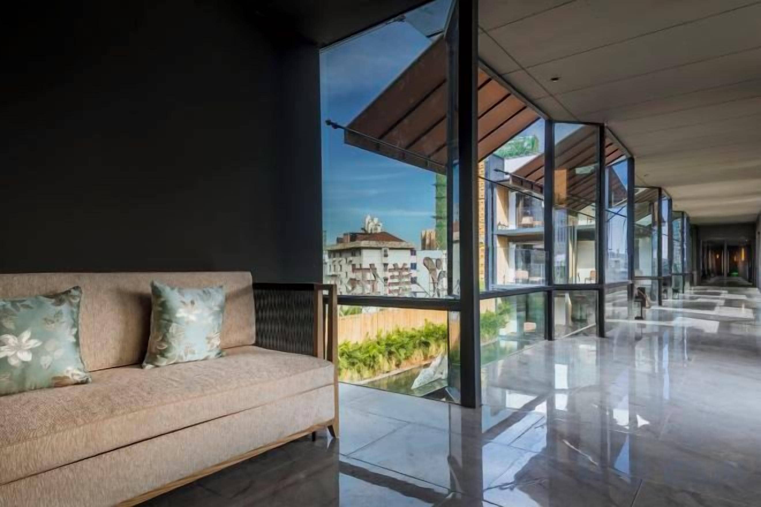 Un intérieur moderne avec un canapé et de grandes fenêtres donnant sur des immeubles.