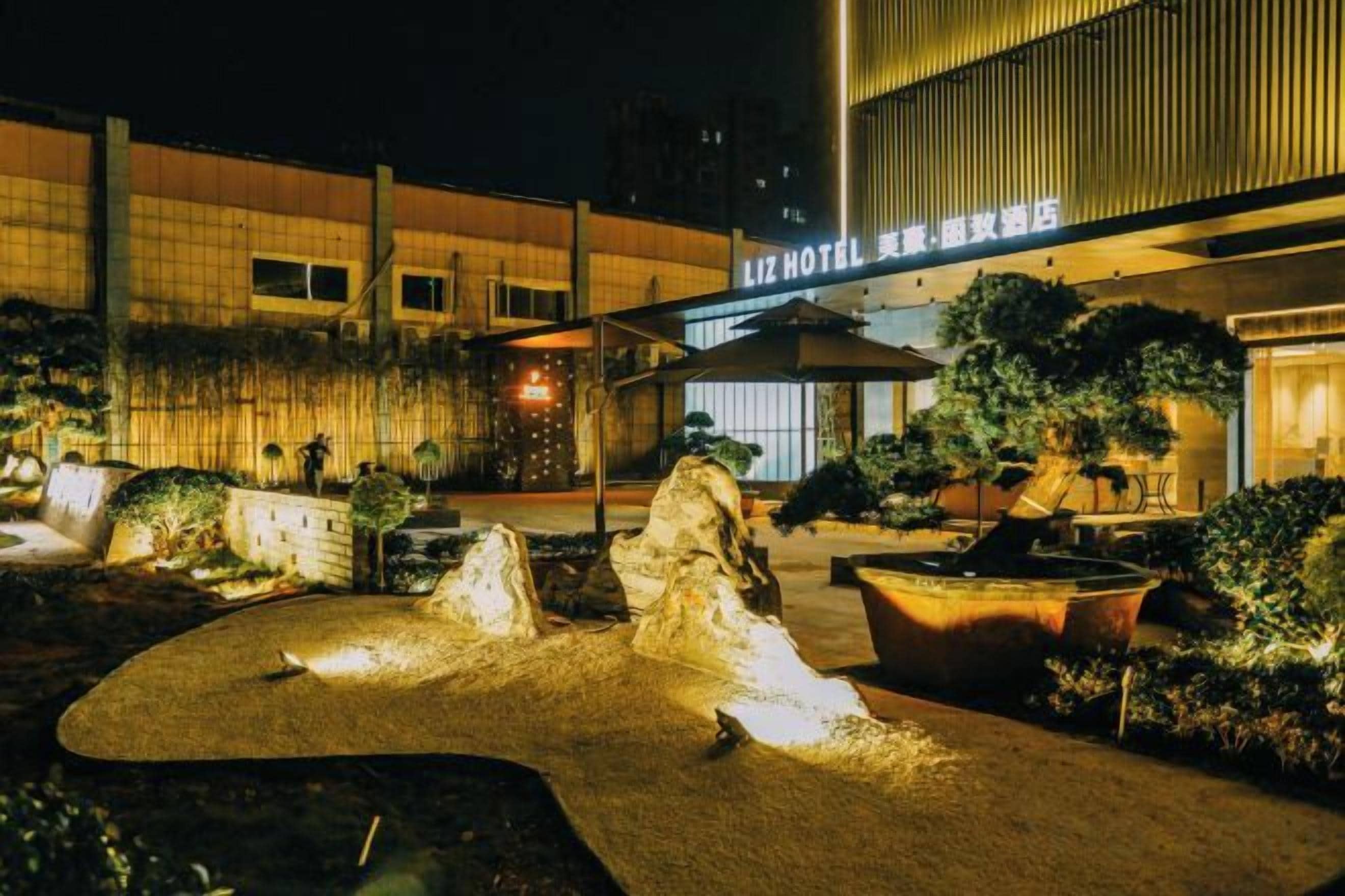 Entrada de hotel con un camino bien iluminado, zona de estar al aire libre y un edificio con señalización.