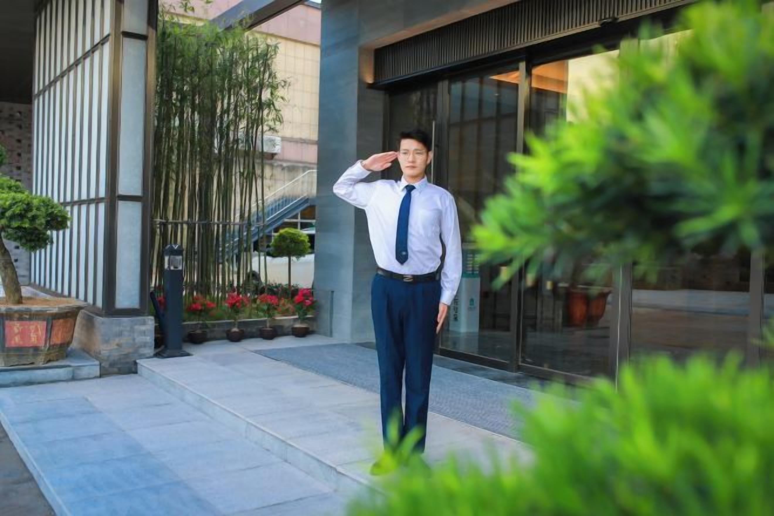 A person standing in front of a building with a modern design, a staircase, and potted plants.