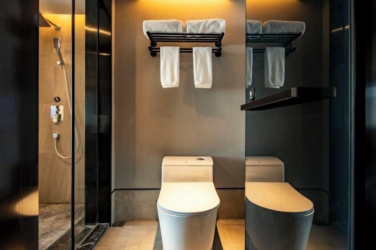 A modern bathroom with two toilets, a shower, and a towel rack with towels.