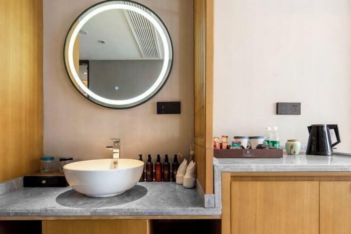 A modern bathroom with a round mirror, a vessel sink, and a coffee maker on the counter.