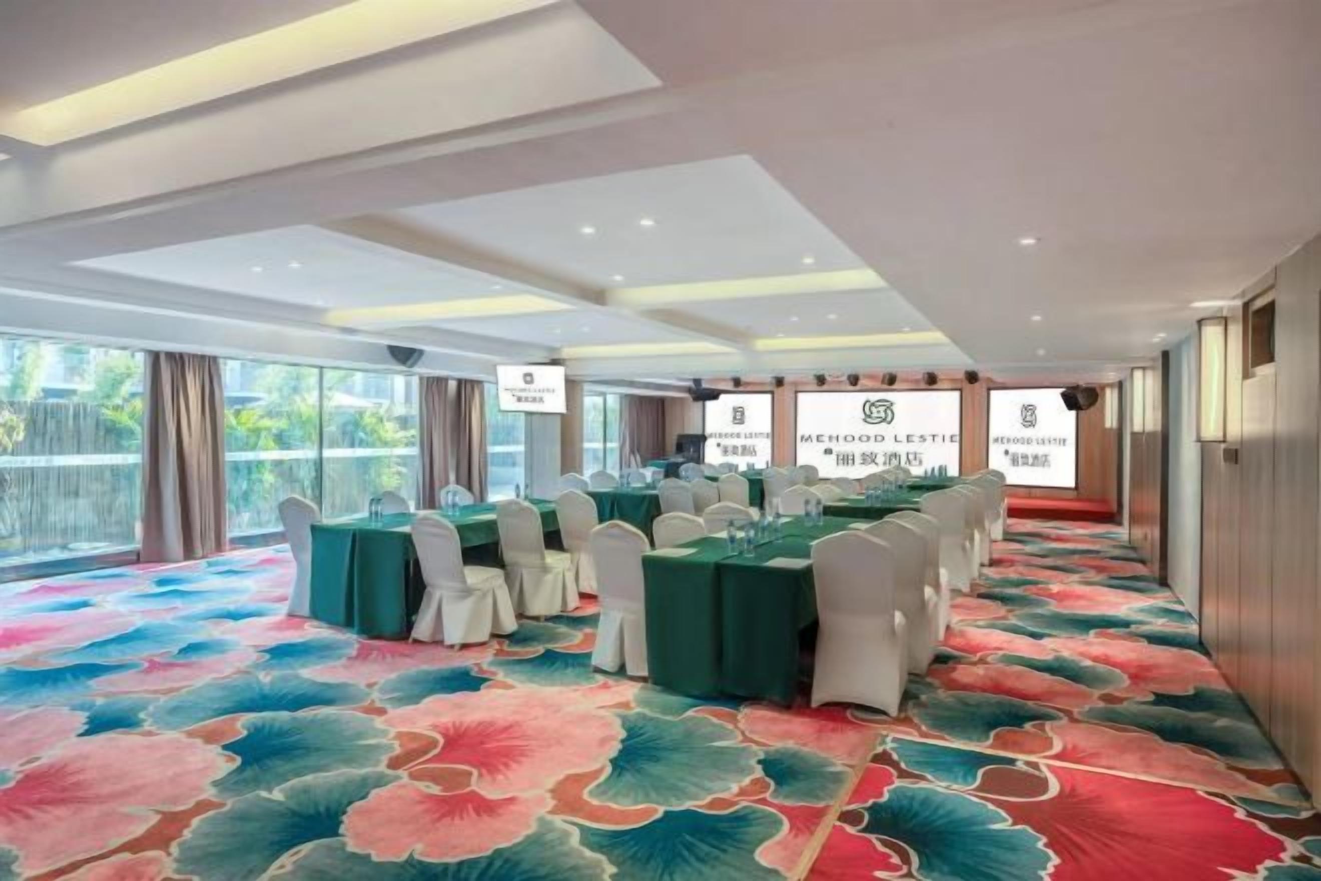 Un salón de conferencias con mesas y sillas, ventanas amplias y una alfombra estampada.