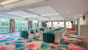Un salón de conferencias con mesas y sillas, ventanas amplias y una alfombra estampada.