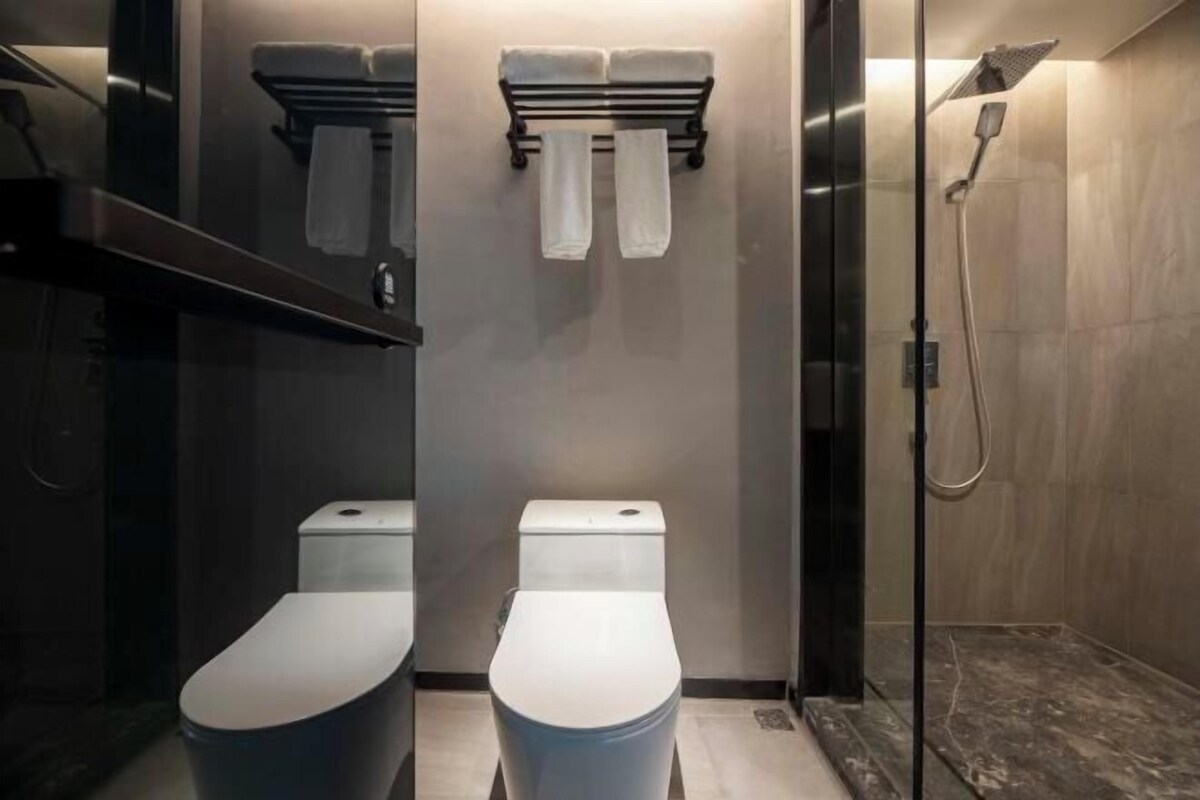 A modern bathroom with two toilets, a shower, and a towel rack.
