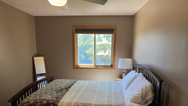 Un dormitorio con cama, ventana, mesita de noche y lámpara.