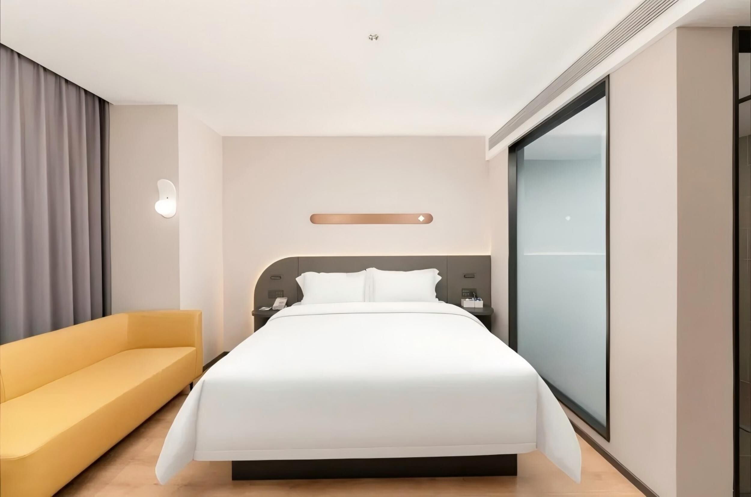 Una habitación de hotel moderna con cama, sofá, mesita de noche y un amplio ventanal.