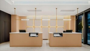A reception area with two reception desks, a modern light fixture, and a patterned wall. - Jinjiang Inn (Wuhan)