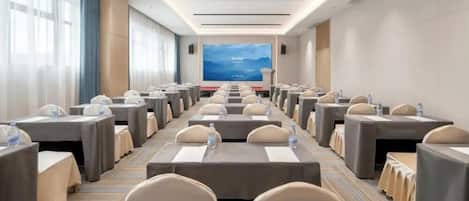 A conference room with rows of tables and chairs, a large screen at the front, and a carpeted floor.