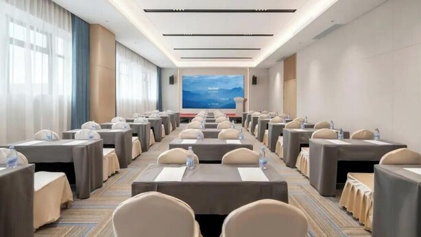 A conference room with rows of tables and chairs, a large screen at the front, and a carpeted floor. - Jinjiang Inn (Wuhan)