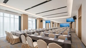 A conference room with rows of tables and chairs, large windows, and a flat-screen TV mounted on the wall. - Jinjiang Inn (Wuhan)