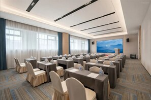 Un salón de conferencias con filas de mesas y sillas, una pantalla grande y piso alfombrado.