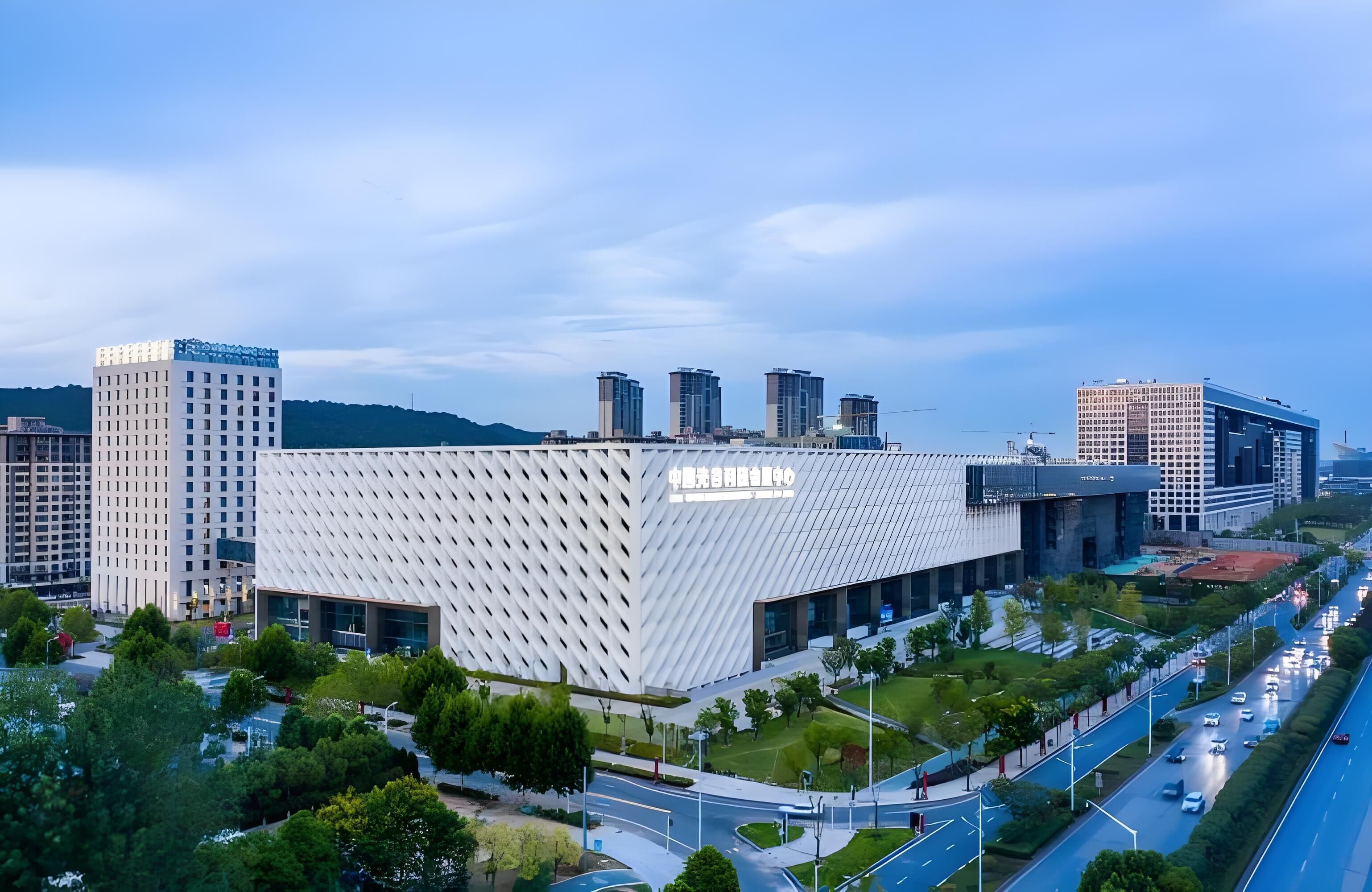 Un bâtiment moderne doté d’une façade géométrique originale, entouré d’un paysage urbain bien aménagé, avec des routes et des espaces verts.