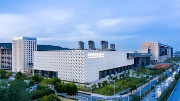 A modern building with a unique geometric facade, surrounded by a well-maintained urban landscape with roads and greenery.