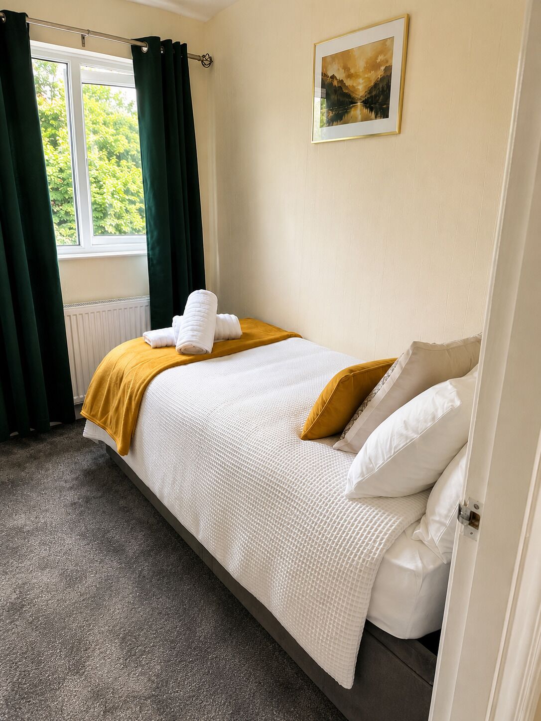 A bedroom with a bed, a window with curtains, a radiator, and a painting on the wall.